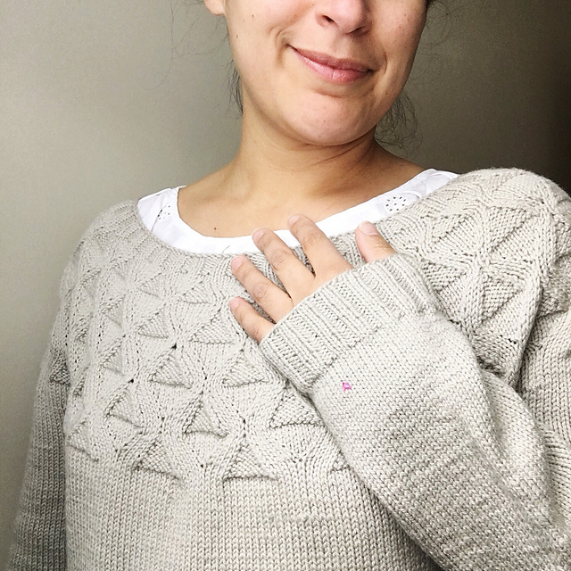 Margaux in a cream Kirigami sweater holding up one asm to show a contrasting duplicate Rare Stitch